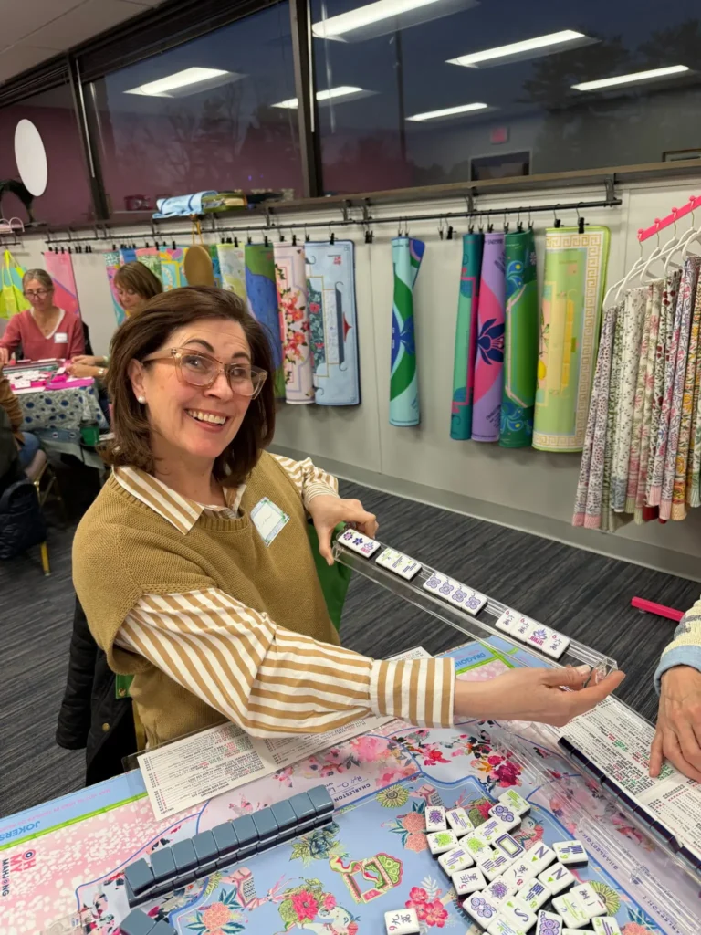 Woman in a gold sweater holding a mahjong rack of tiles